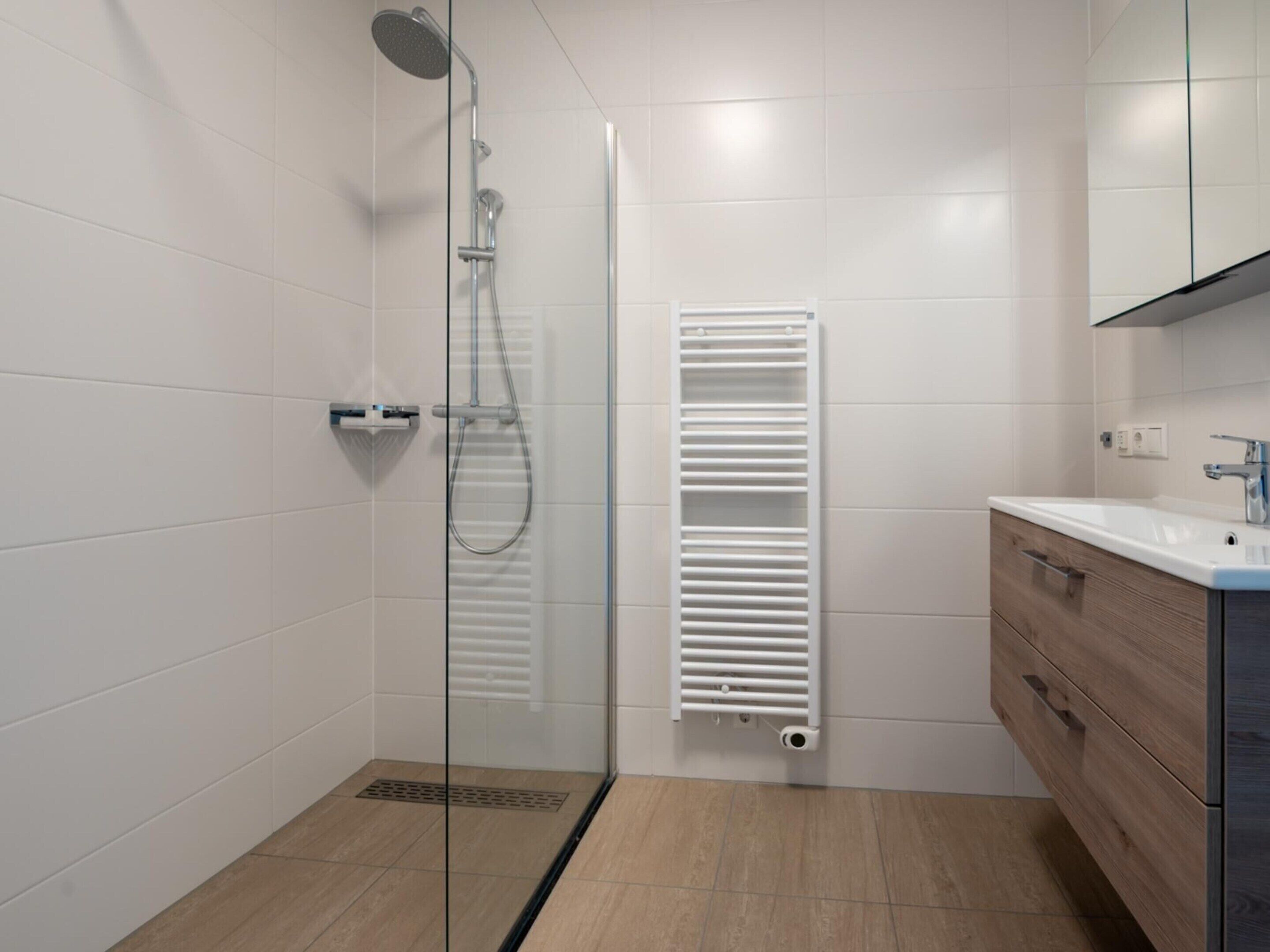 A modern bathroom with a glass shower enclosure, a white towel rack, and a wooden vanity with a mirror.