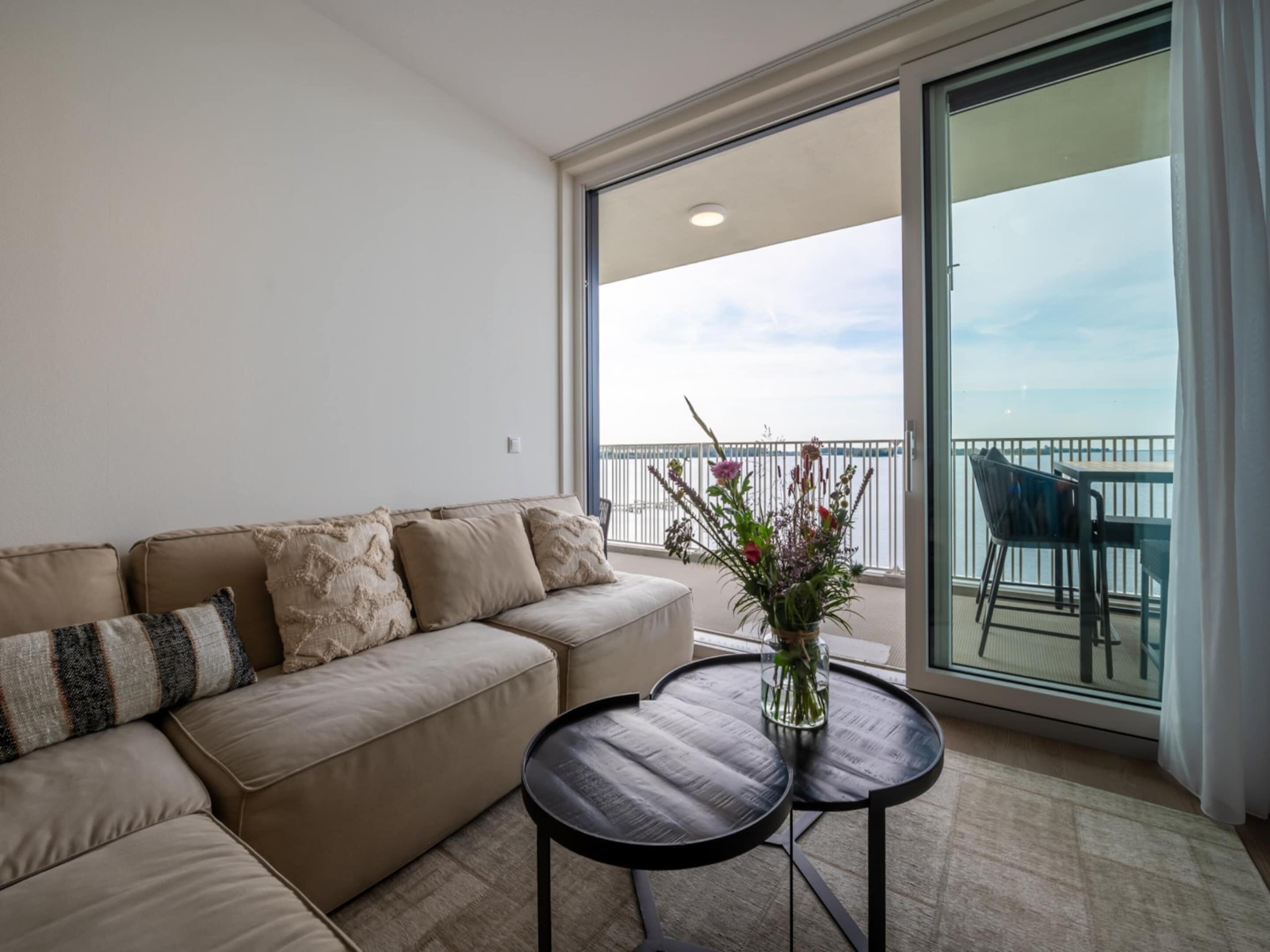 A balcony with a view of the sea, a sofa, and two small tables.