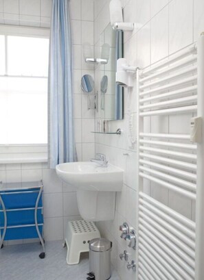 Ein Badezimmer mit Waschbecken, Spiegel, Handtuchhalter, Duschvorhang, blauem Badstuhl, Mülleimer und Radiator.