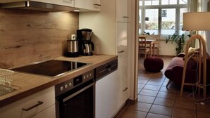 Una cocina moderna con horno empotrado, cafetera y comedor con una silla roja y una mesa.