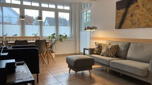 Una sala de estar con un sofá, un reposapiés y una zona de comedor con sillas y una mesa.