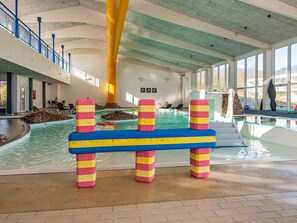Une piscine intérieure agrémentée de séparations colorées, d’un mur en pierre et offrant une vue sur l’extérieur grâce à de grandes fenêtres.