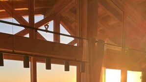 Une pièce dotée de grandes fenêtres, d’un plafond en bois et offrant une vue sur un paysage enneigé au coucher du soleil.