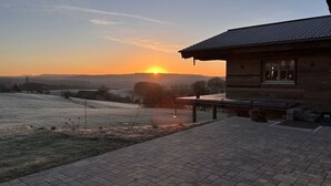 Un bâtiment rustique, doté d’un toit en tuiles et d’une fenêtre, qui donne sur un champ gelé au coucher du soleil.