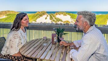 Una pareja sentada en una mesa de madera con vista a la playa y las dunas.