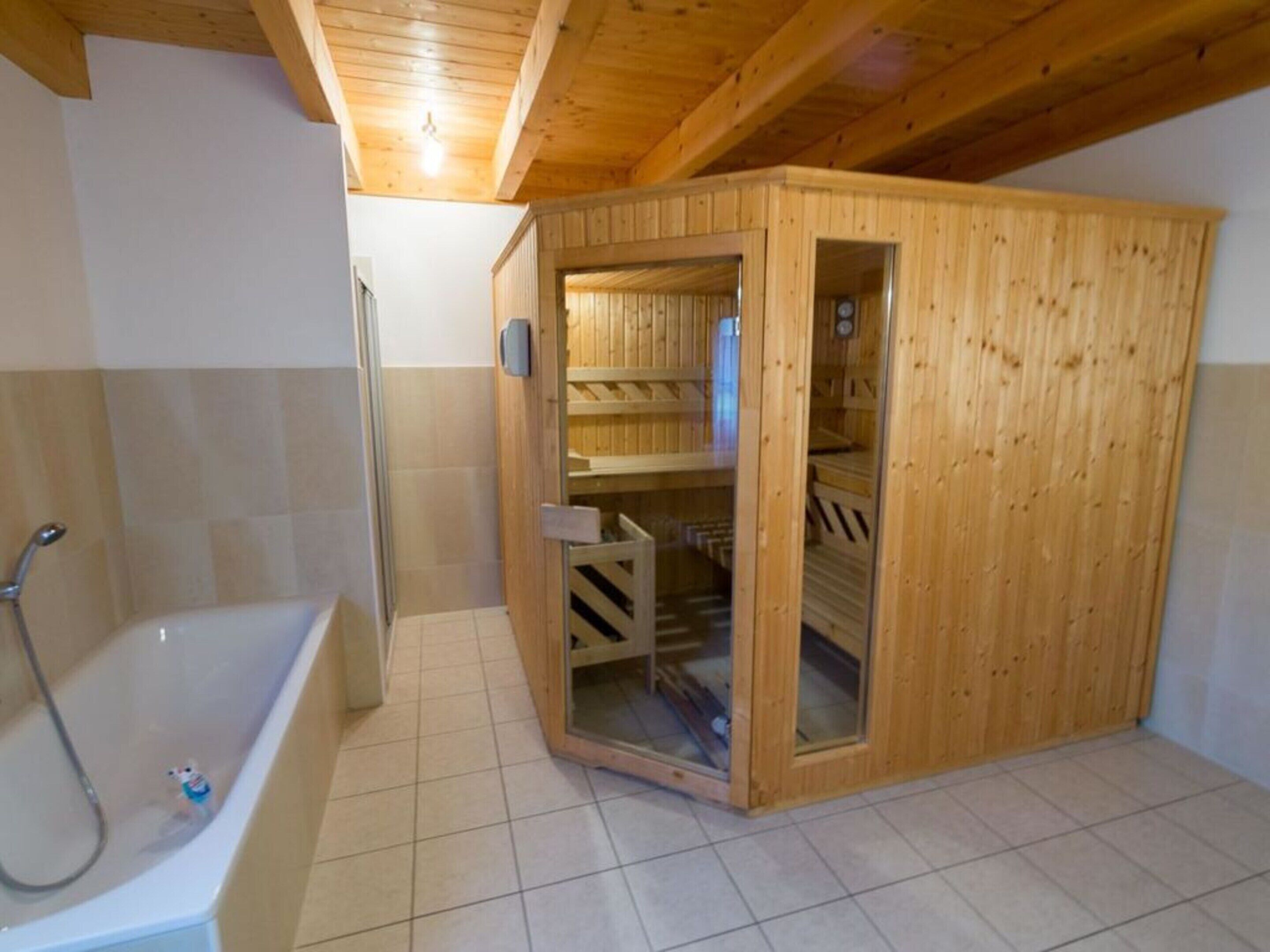 A sauna room with a wooden door, a glass door leading to a shower area, and a bathtub.