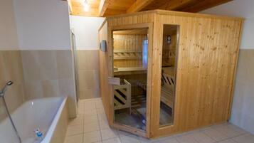 A sauna room with a wooden door, a glass door leading to a shower area, and a bathtub.