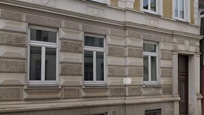 Une façade d’immeuble avec des fenêtres rectangulaires, des éléments décoratifs en pierre et une porte.