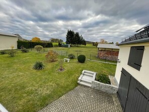 Una propiedad residencial con un patio pavimentado, un pequeño jardín con diversas plantas, una valla de madera y un cobertizo.