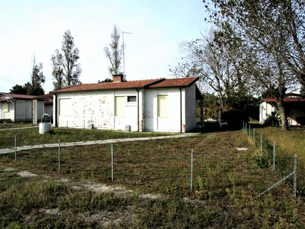 A small, single-story house with a red-tiled roof, white walls, and a front yard with a fence.