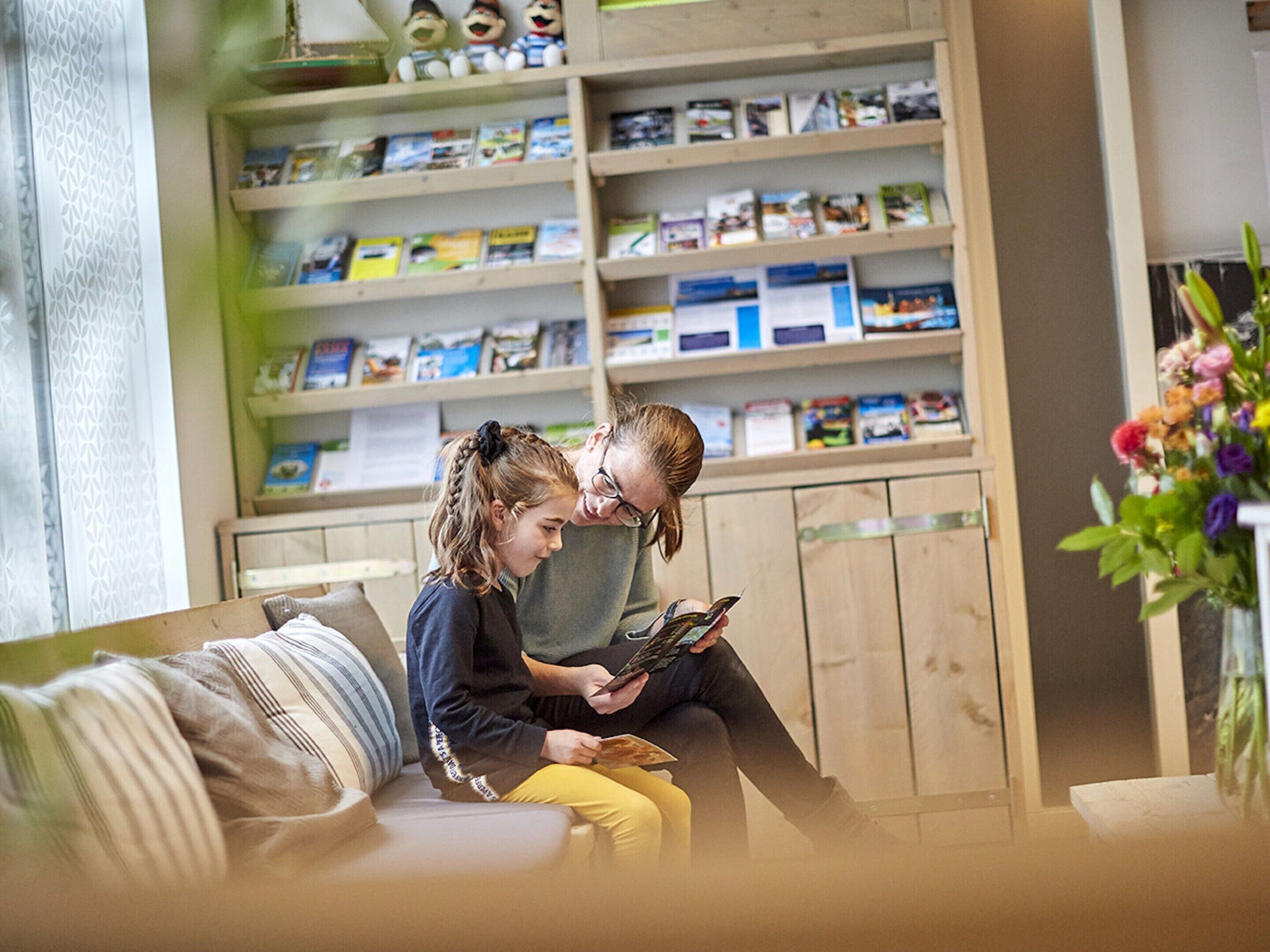 Een gezellige woonkamer met een houten boekenkast vol boeken en tijdschriften, een comfortabele bank en een vaas met bloemen.
