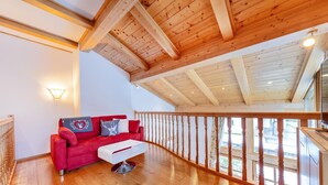 Una habitación amplia con techo de madera, un sofá rojo, una mesa de centro blanca y una barandilla de madera con vistas.
