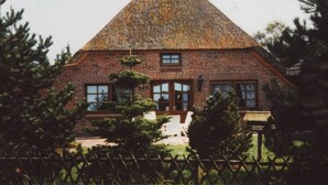 Une maison traditionnelle en briques, dotée d’un toit à forte pente, entourée d’une clôture en bois et d’arbres.