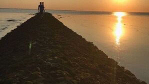 Une longue jetée étroite qui s’avance dans des eaux calmes au coucher du soleil.