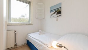 Un dormitorio pequeño y ordenado con una cama individual, una ventana, un radiador y un cuadro colgado en la pared.