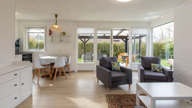 Una cocina moderna con armarios blancos, una mesa de comedor y sillas. Hay dos sofás con cojines y una mesa baja blanca.
