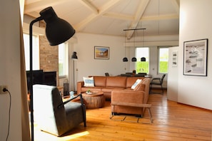A spacious living room with a leather sofa, a round coffee table, and a black floor lamp. - Nice House on the Golf Course With Sauna (Hollum)