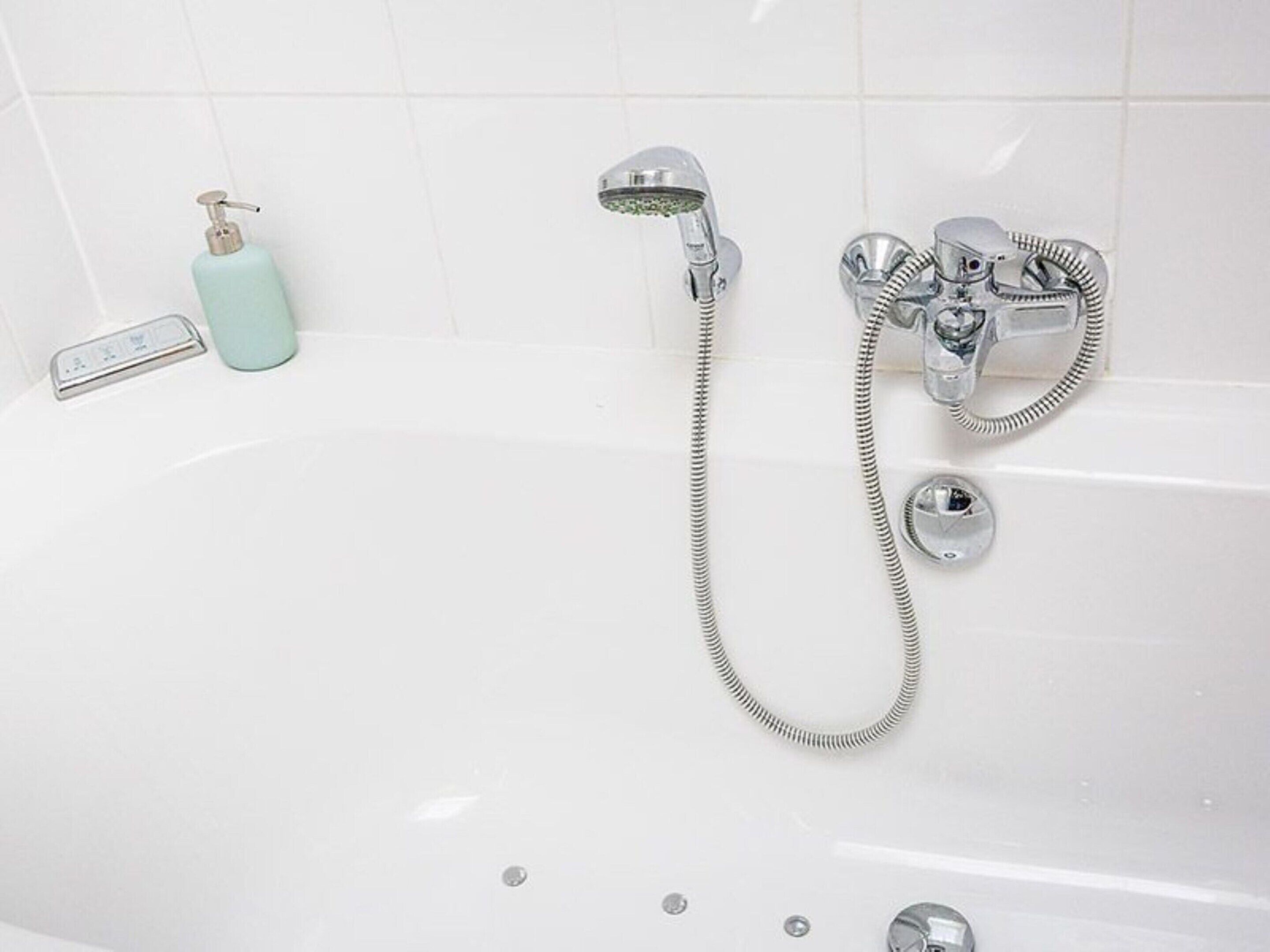 Une baignoire blanche dotée d’un pommeau de douche à main et d’un robinet intégré.