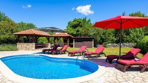 A swimming pool with lounge chairs and umbrellas, surrounded by stone tiles and greenery. - Villa Tara With a Beautiful Heated Pool (Dobrinj)