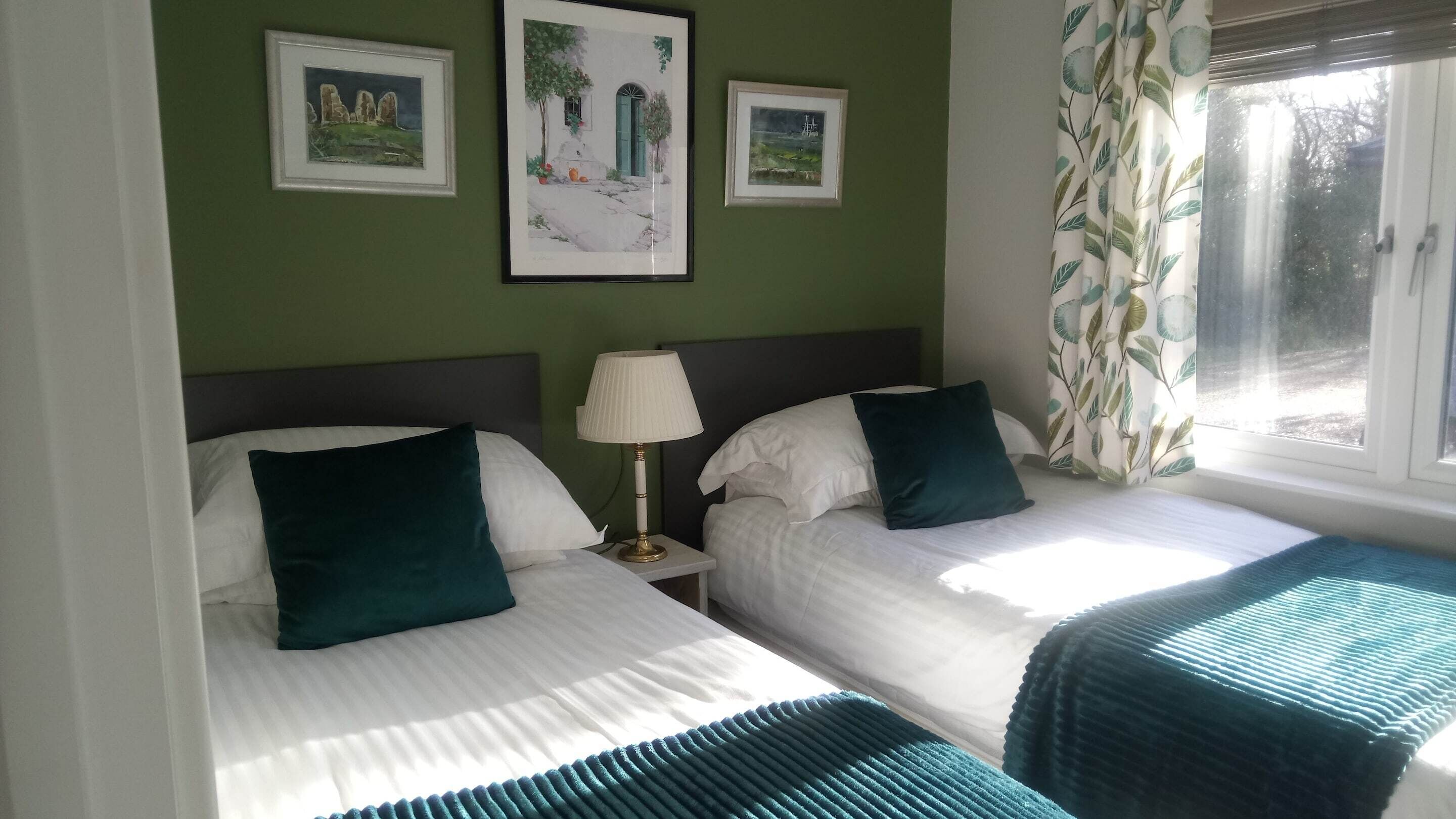 A room with two beds, a nightstand with a lamp, and three framed pictures on the wall.