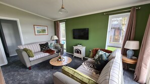 A living room with a sofa, armchair, and a coffee table. There is a television mounted on the wall and a window with curtains. - Cottage in Brookland Near Romney Marsh Beach (Romney Marsh)