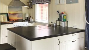 A compact kitchen with a black countertop, white cabinets, a stove, and a window with blinds. - 8 Person Holiday Home in Klokkarstua (Asker)
