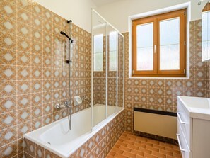 Un bagno con piastrelle decorate, una vasca da bagno, una doccia e una finestra con vetro satinato.