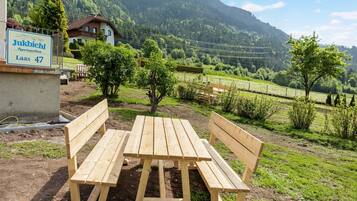 Un banc en bois et une table de pique-nique dans un cadre rural, avec une pancarte indiquant : « Jukbichl Appartementhaus Laas 47 ».