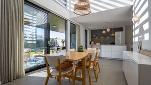 A modern kitchen with white cabinets, a wooden dining table, and a view of the outdoors.