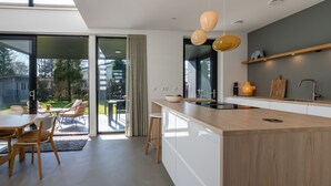A modern kitchen with a large island, pendant lighting, and a sliding glass door leading to an outdoor patio.