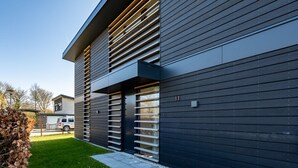 A modern building with horizontal wooden slats, a paved driveway, and a clear sky.
