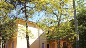 Um edifício amarelo com várias janelas e portas, rodeado de árvores e um espaço gramado.