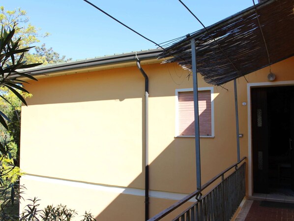 A building with a yellow exterior, a window with a wooden shutter, and a metal railing.