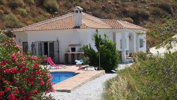 Une villa blanche avec un toit en tuiles, une piscine et un espace salon extérieur.