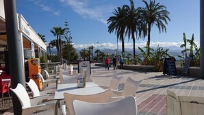 Un café en plein air avec des chaises et des tables en plastique blanc, un distributeur automatique et un panneau indicateur.