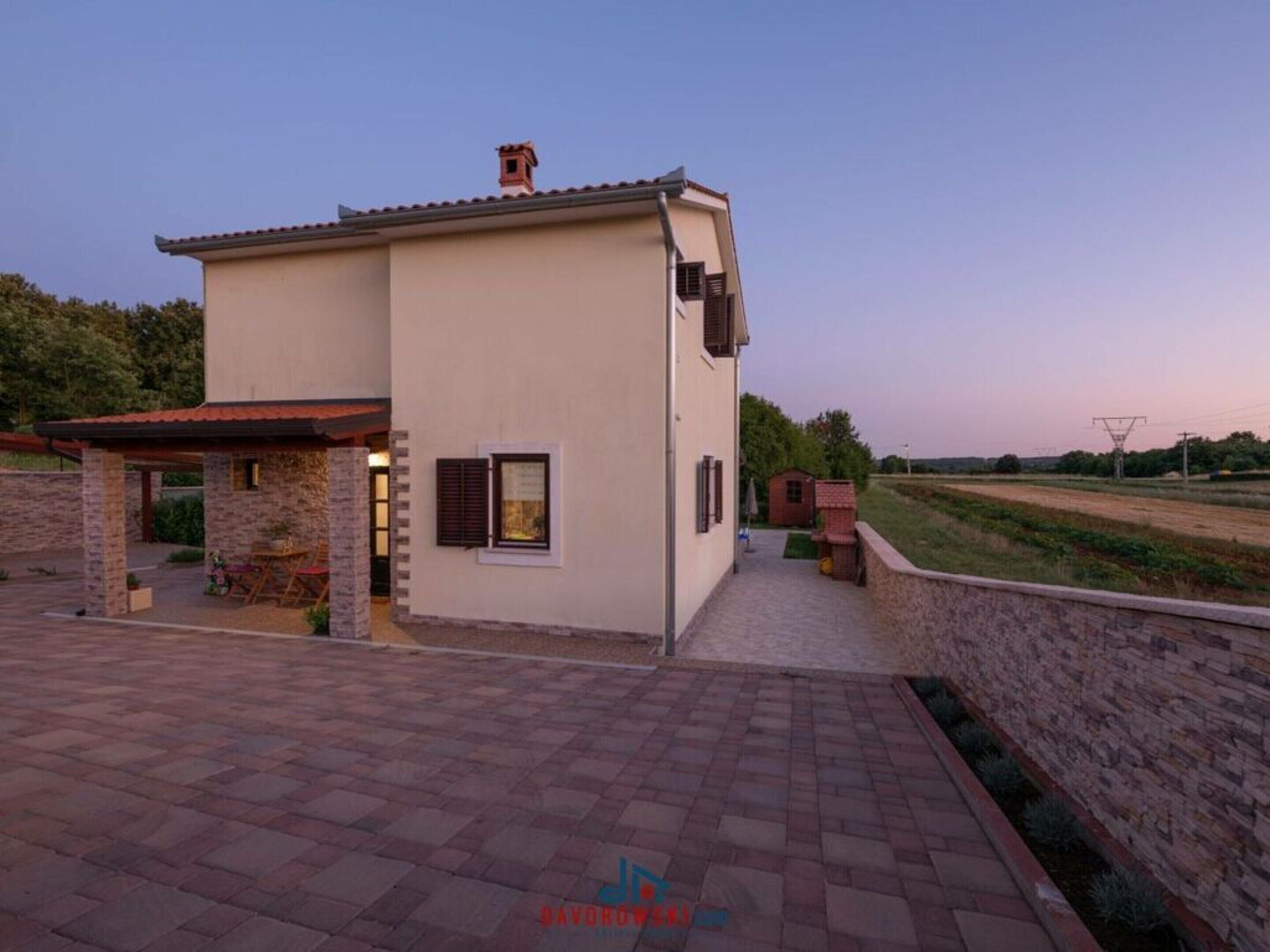 A two-story building with a flat roof, a small attached structure, and a paved patio area.