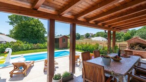 An outdoor patio with a wooden pergola, a pool, lounge chairs, and a table with fruit and a bottle. - Madonnina Comfortable Holiday Residence (Barban)