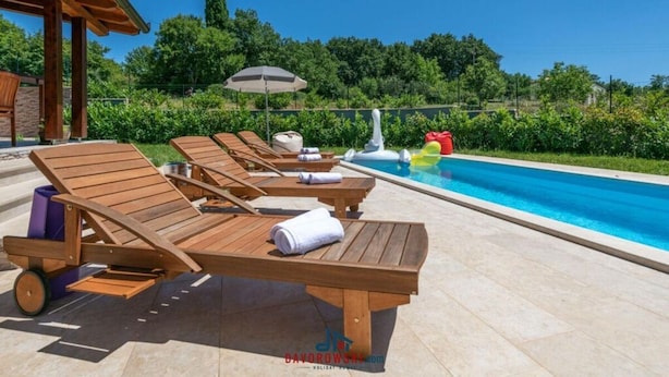 A poolside area with wooden lounge chairs, a small inflatable float, and a covered seating area. - Madonnina Comfortable Holiday Residence (Barban)