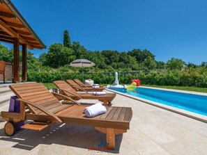 A poolside area with wooden lounge chairs, a small inflatable float, and a covered seating area. - Madonnina Comfortable Holiday Residence (Barban)
