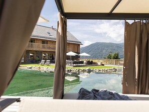 A bedroom with a view of a pool, outdoor seating, and a mountain backdrop. - Nice Chalet in Wolting With Natural Swimming Pond (Tamsweg)