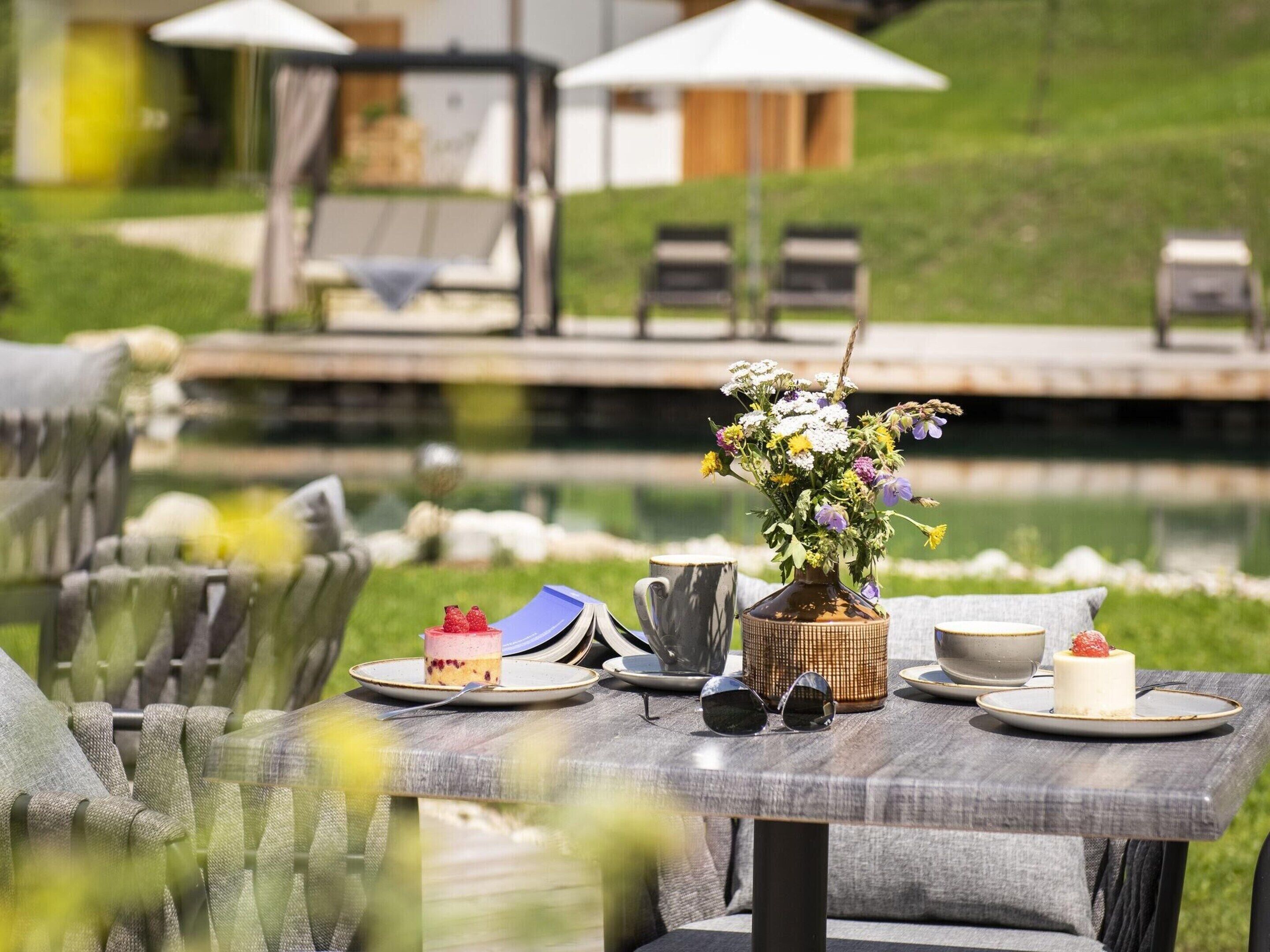 A dining table with a vase of flowers, a cake, and a cup.