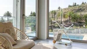 Une chambre moderne dotée de grandes fenêtres, d’une piscine et offrant une vue sur un paysage vallonné.