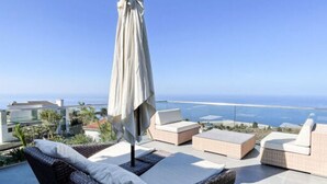 Une terrasse sur le toit, aménagée avec des meubles en osier et dotée d’un grand parasol, offrant une vue imprenable sur la côte.
