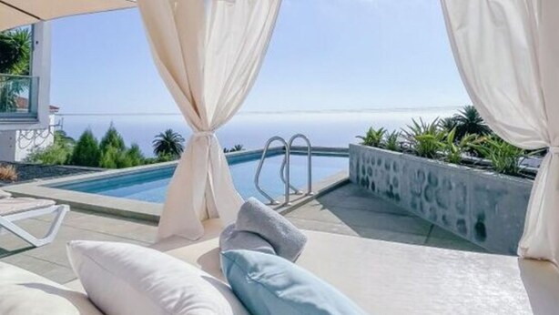 Une terrasse sur le toit avec une piscine, des coussins blancs et une vue sur la mer.