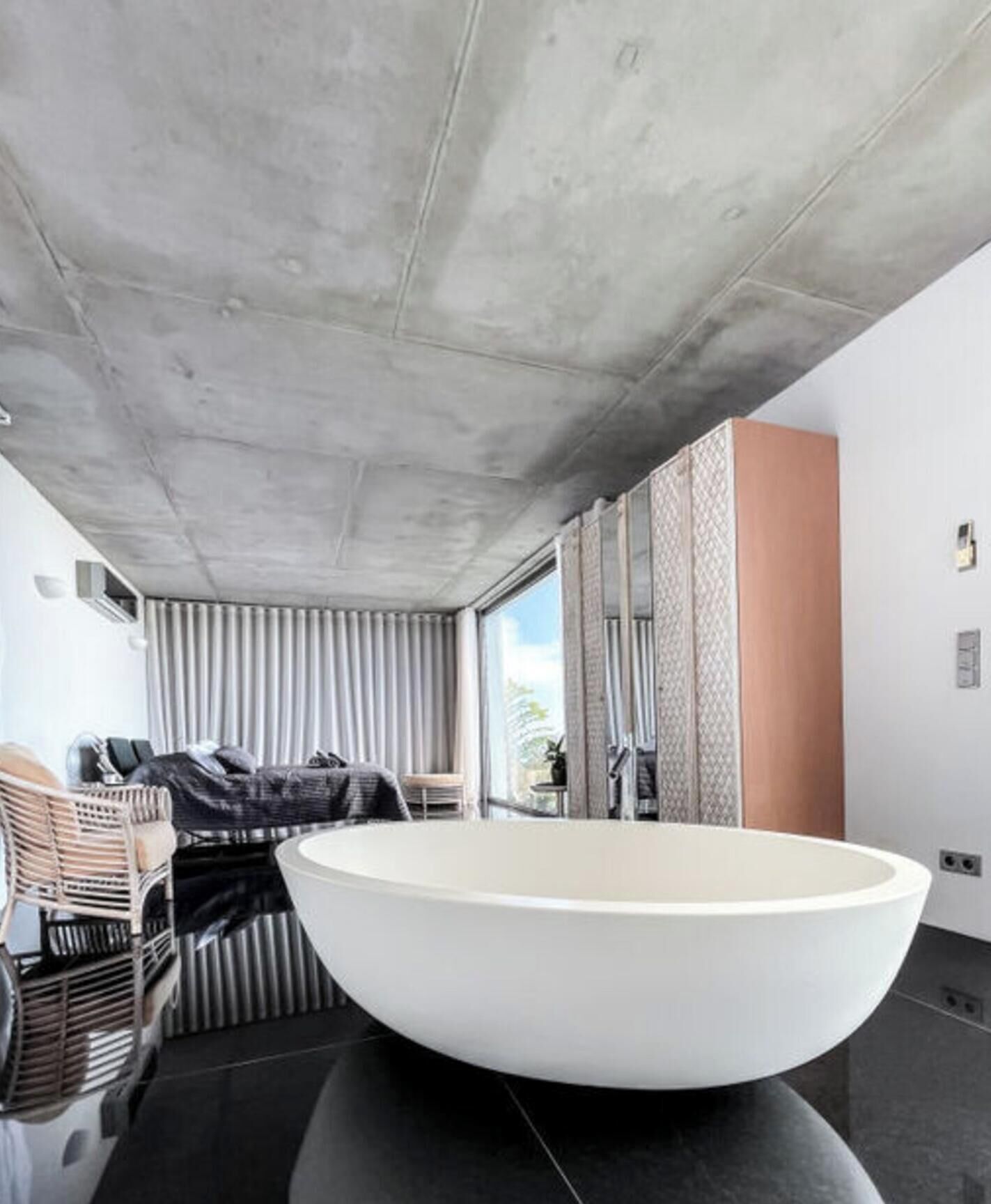 Een moderne badkamer met een groot bad, een zithoek met een stoel en een klein tafeltje, en uitzicht op de omgeving door grote ramen.