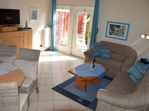 Relax in this stylish living room with a sofa set, dining table, and TV on a cabinet, plus a sliding door leading to an outdoor view.