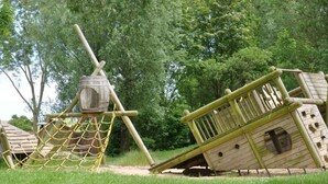 Une structure de jeu en bois, dotée d’un filet en corde et d’un objet en forme de tonneau.
