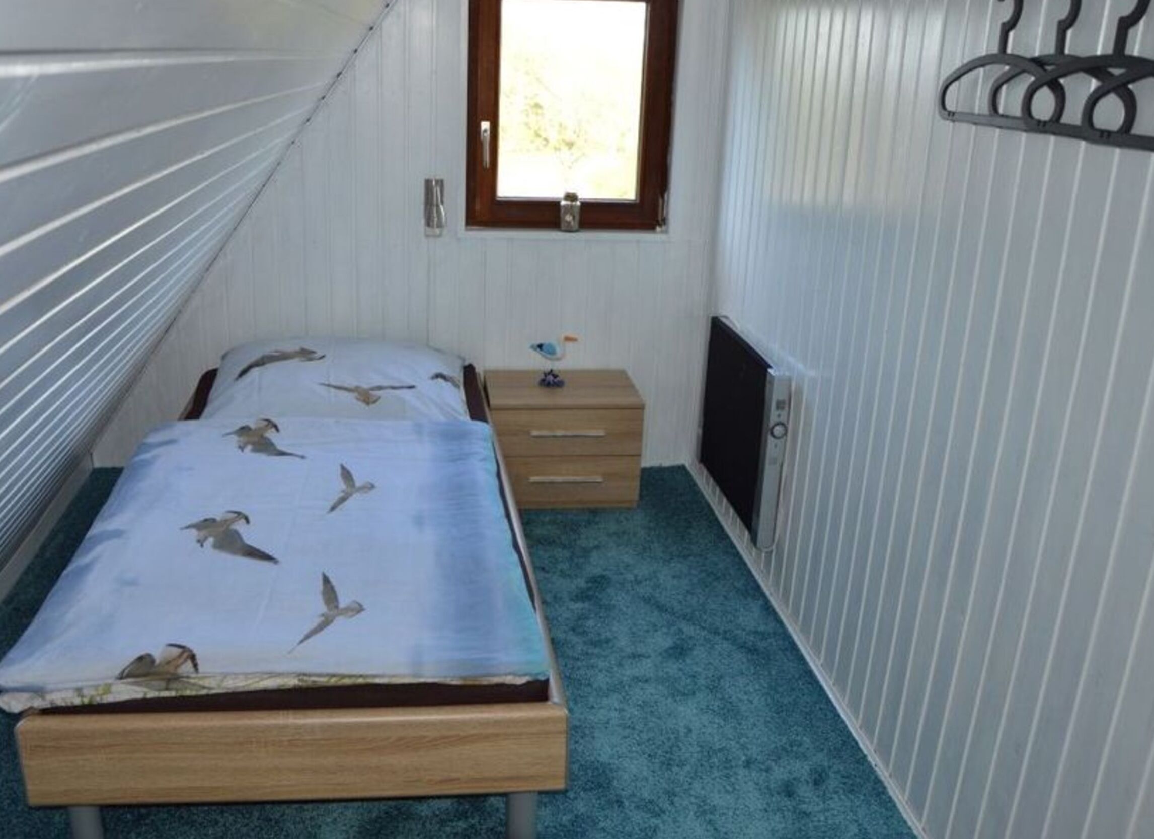 Una habitación pequeña y funcional con una cama nido, un pequeño tocador, un calefactor y una ventana con persianas.