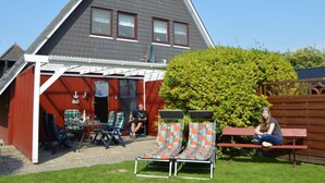 Une maison avec un toit en pente, un patio couvert avec des meubles d’extérieur et une pelouse bien entretenue.