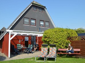 Relax in the comfort of this charming home, featuring a gabled roof and a cozy outdoor space with lounge chairs and a bench.